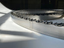Multiple band saw blades displayed in a grouping, on a white backdrop with a dark background. 1.25" wide, 7/8" tooth spacing, with a 10 degree hook angle. Big Mouth Blades is the supplier for these portable sawmill blades.
