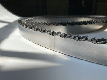 Multiple band saw blades displayed in a grouping, on a white backdrop with a dark background. 1.25" wide, 7/8" tooth spacing, with a 10 degree hook angle. Big Mouth Blades is the supplier for these portable sawmill blades.