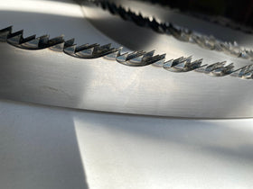 Multiple band saw blades displayed in a grouping, on a white backdrop with a dark background. 1.25" wide, 7/8" tooth spacing, with a 10 degree hook angle. Big Mouth Blades is the supplier for these portable sawmill blades.