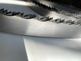 Multiple band saw blades displayed in a grouping, on a white backdrop with a dark background. 1.25" wide, 7/8" tooth spacing, with a 10 degree hook angle. Big Mouth Blades is the supplier for these portable sawmill blades.