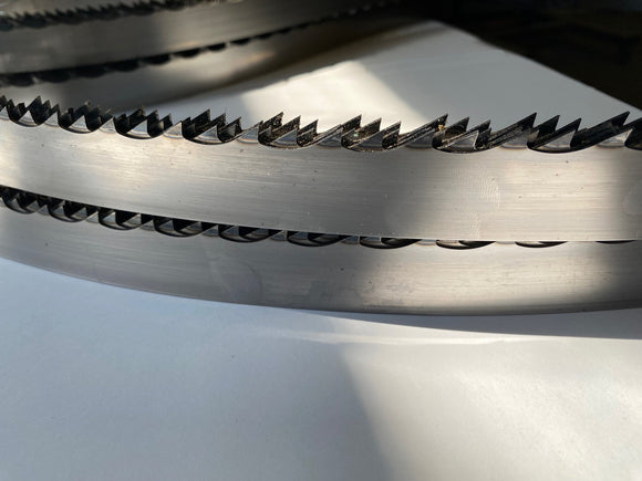 Multiple layers of band saw blades displayed in a grouping, on a white backdrop with a dark background. 1.25" wide, 7/8" tooth spacing, with a 10 degree hook angle. Big Mouth Blades is the supplier for these portable sawmill blades.