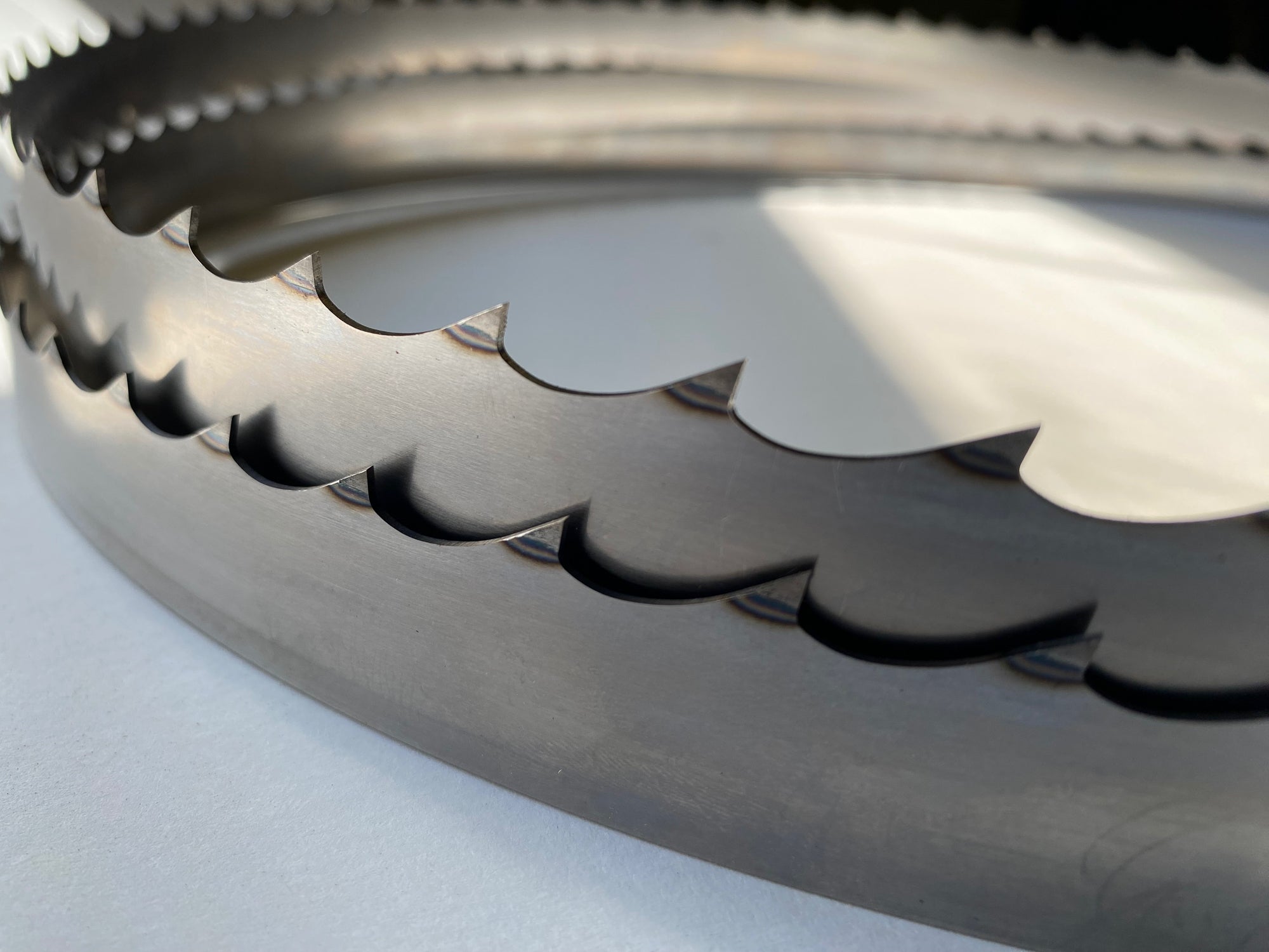 Multiple band saw blades displayed in a grouping, on a white backdrop with a dark background. 1.5" wide, 7/8" tooth spacing, with a 10 degree hook angle. Big Mouth Blades is the supplier for these portable sawmill blades.