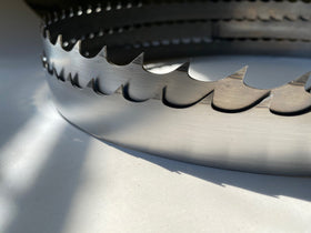 Multiple band saw blades displayed in a grouping, on a white backdrop with a dark background. 2" wide, 1" and 1-1/8" tooth spacing, with a Deep 7 hook angle. Big Mouth Blades is the supplier for these portable sawmill blades.