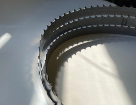 Multiple band saw blades displayed in a grouping, on a white backdrop with a dark background. 2" wide, 1" and 1-1/8" tooth spacing, with a Deep 7 hook angle. Big Mouth Blades is the supplier for these portable sawmill blades.