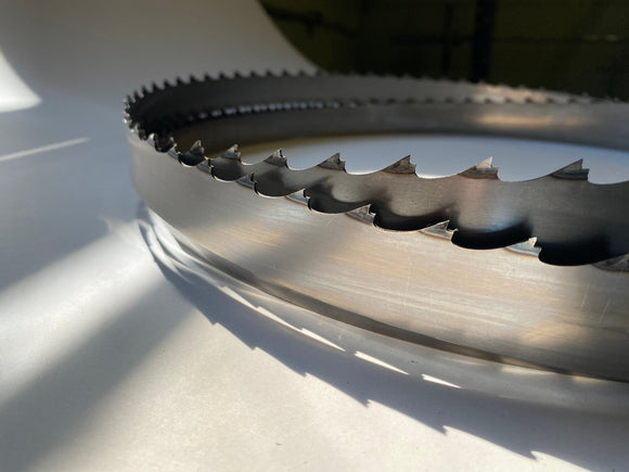 Multiple layers of chip sweep, dust sweep, band saw blades displayed in a grouping, on a white backdrop with a dark background. 1.25" wide, 3/4" tooth spacing, with a 10 degree hook angle. Big Mouth Blades is the supplier for these portable sawmill blades.